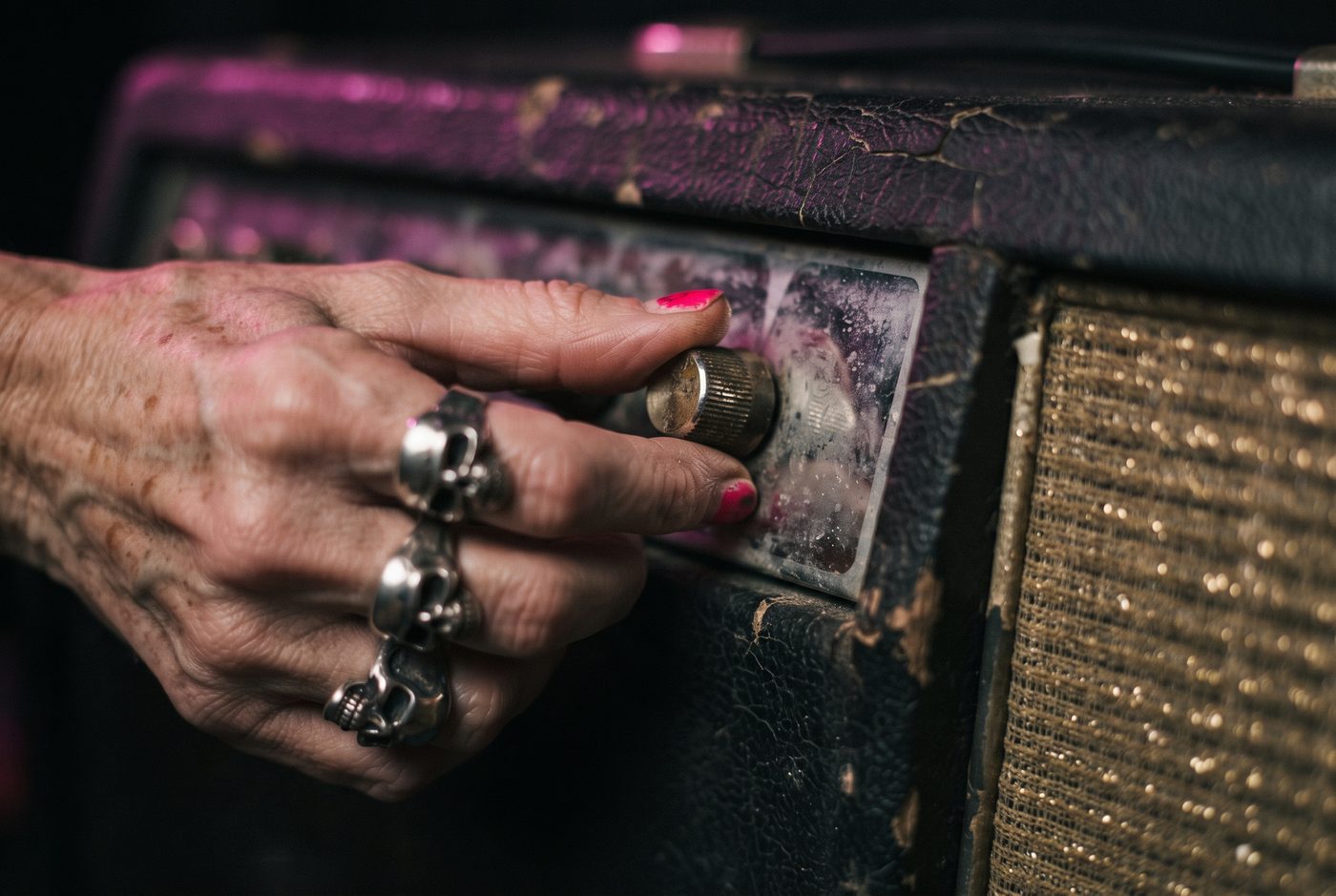 An older hand with silver rings turning an amplifier knob